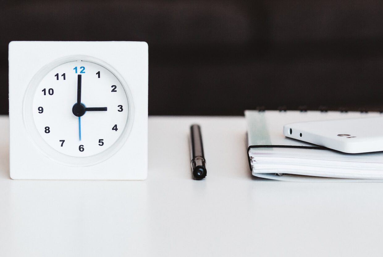 white desk clock near pen and book